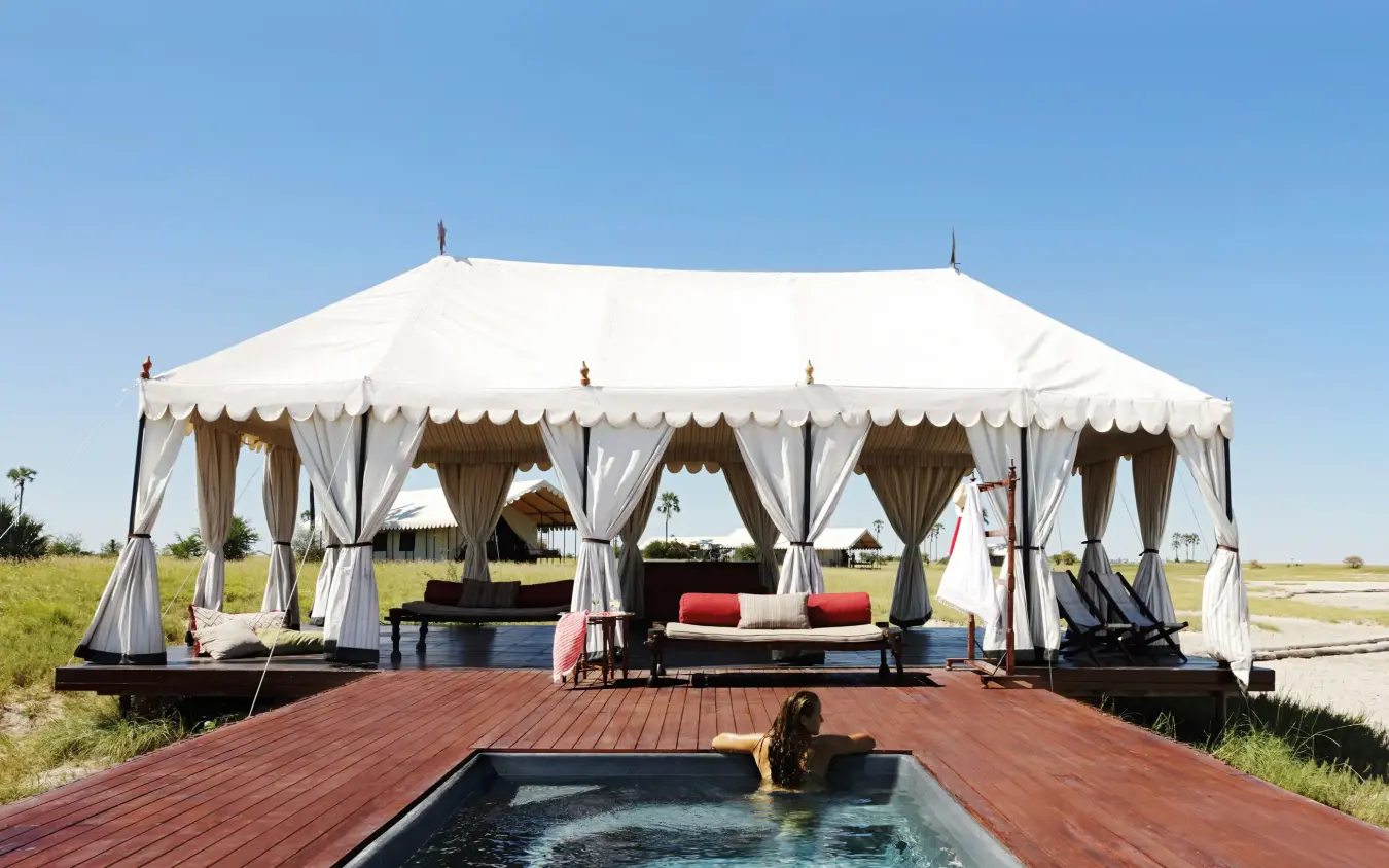 Woman in pool with canvas tent and decking beyond, San Camp, Makgadikgadi Pans, Botswana