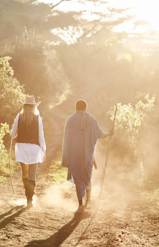 Two guests walking on dusty path through vegetation at sunrise, Sanctuary Crater Camp, Ngorongoro Crater, Tanzania