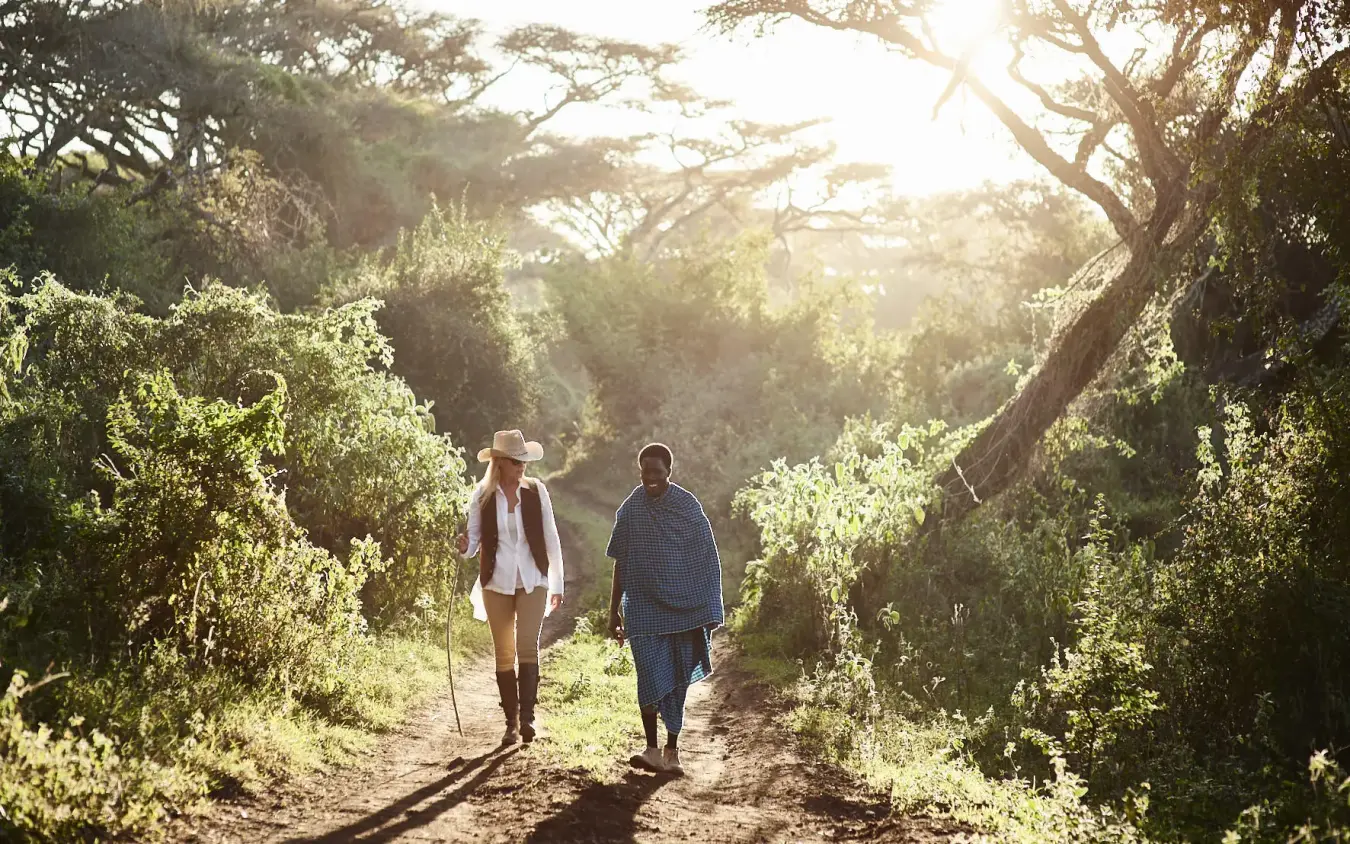 Two guests hiking on tree-lined path during golden hour, Ngorongoro Crater, Tanzania