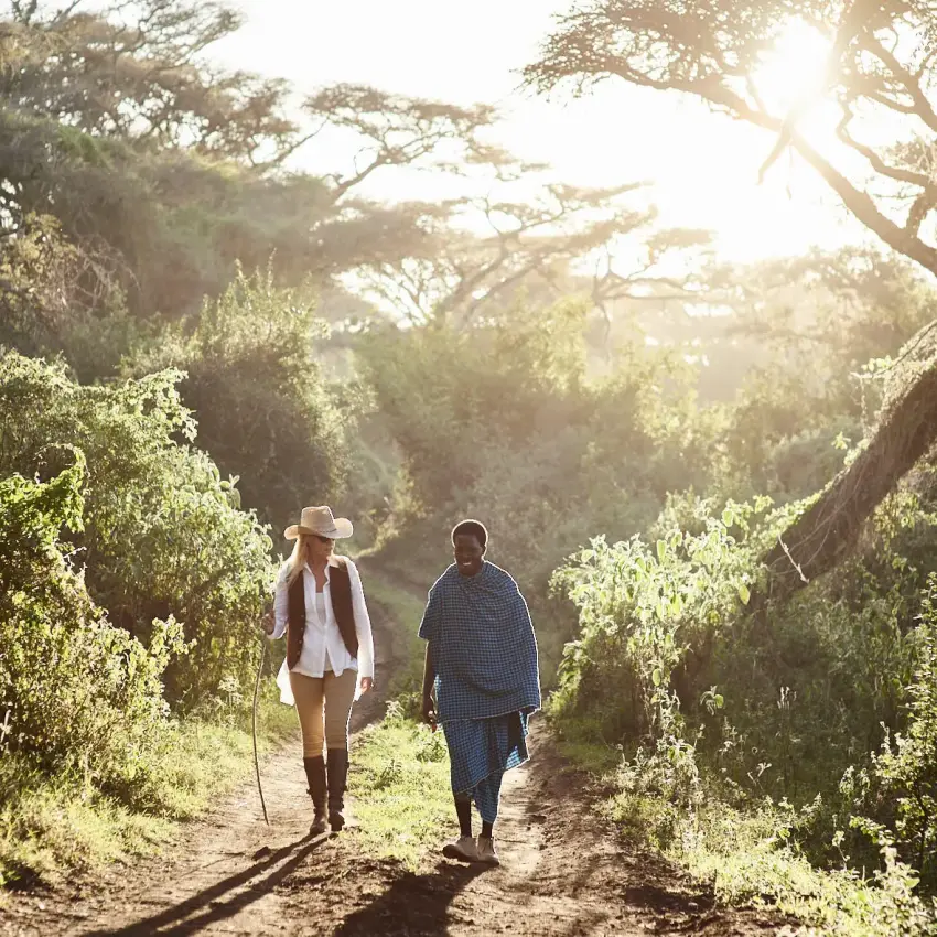 Two guests hiking on tree-lined path during golden hour, Sanctuary Crater Camp, Ngorongoro Crater, Tanzania