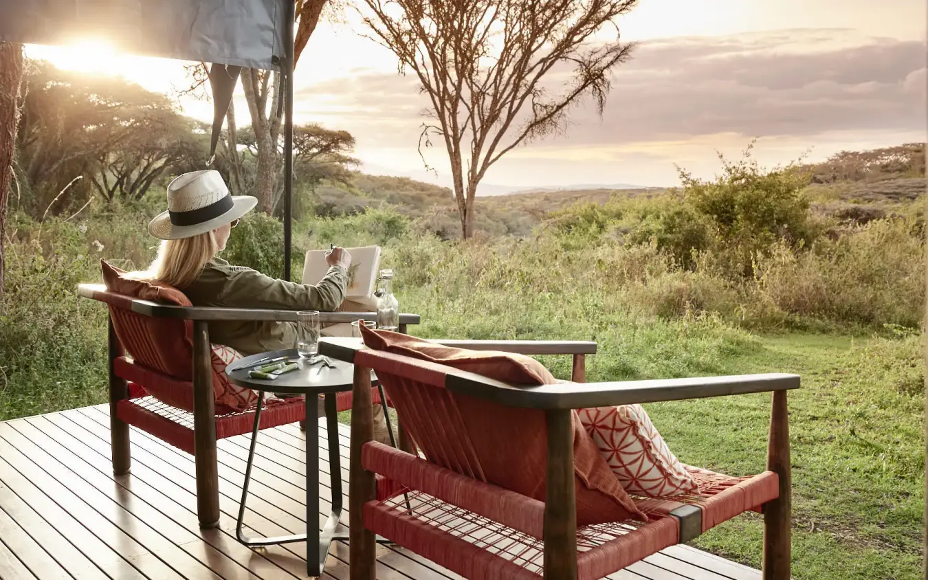 Guest relaxing on wooden deck overlooking savanna landscape, Sanctuary Crater Camp, Ngorongoro Crater, Tanzania