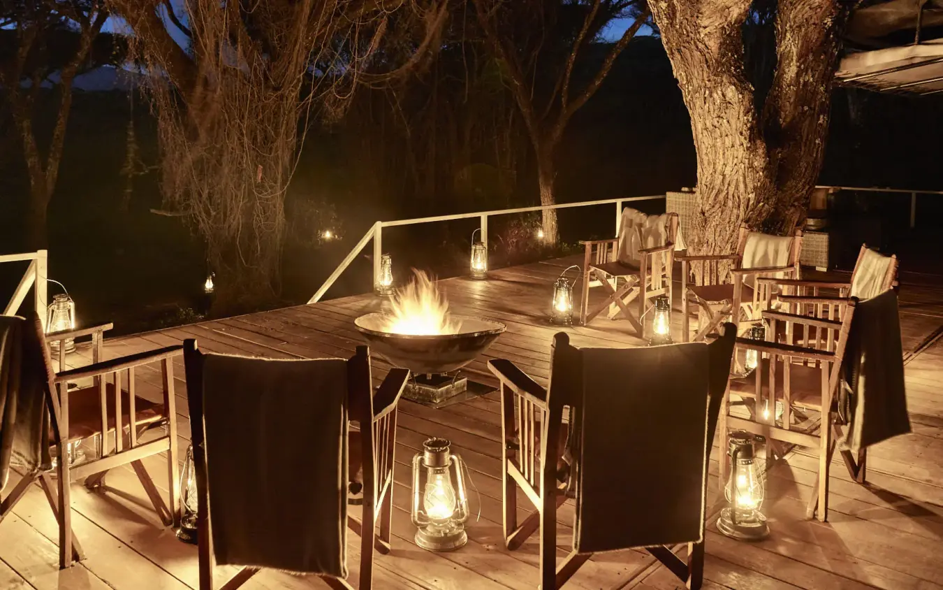 Nighttime deck with fire pit and lantern lighting under trees, Sanctuary Crater Camp, Ngorongoro Crater, Tanzania