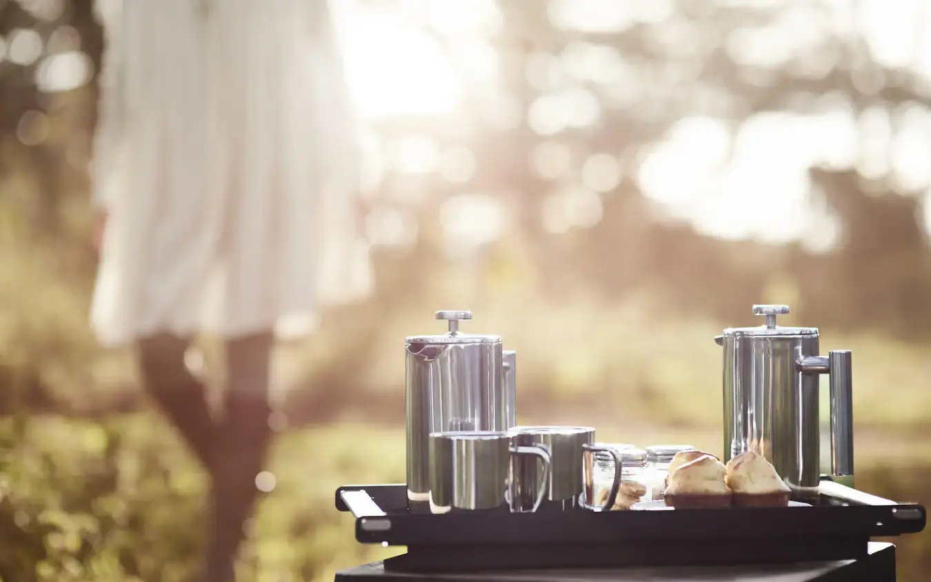 Coffee service setup on table with blurred person outdoors, Sanctuary Crater Camp, Ngorongoro Crater, Tanzania