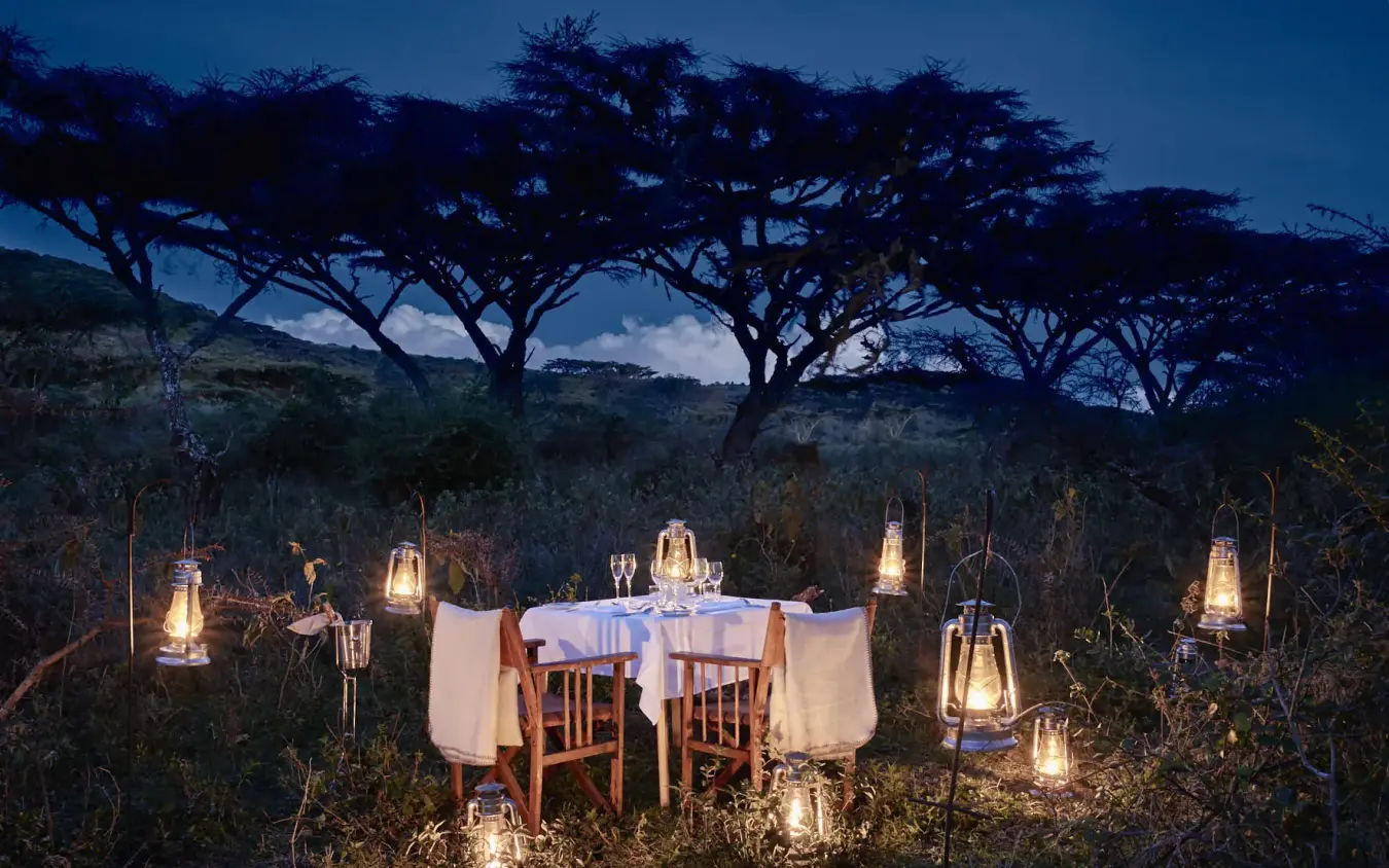 Outdoor dining table set under acacia trees at dusk, Sanctuary Crater Camp, Ngorongoro Crater, Tanzania