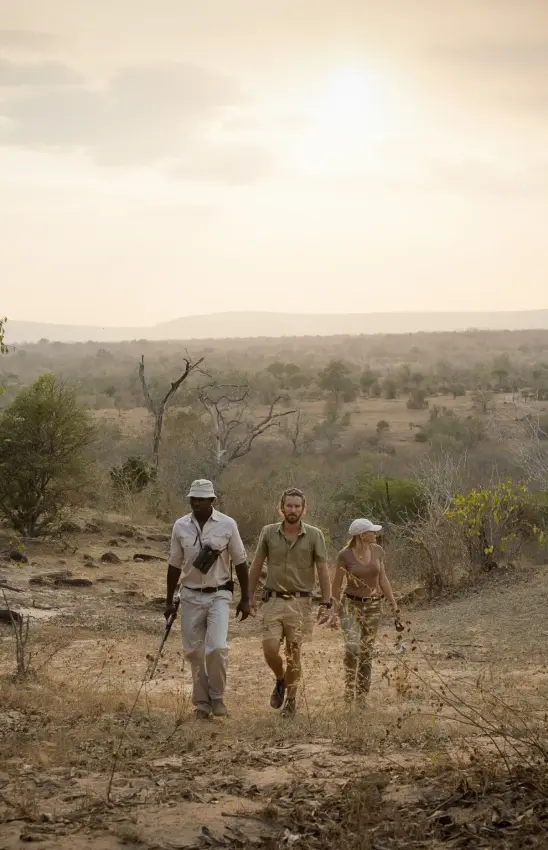 Guides walking through dry bushland with valley landscape in background, Sand Rivers, Nyerere National Park, Tanzania