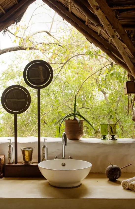 Outdoor bathroom sink with mirrored fixtures overlooking tree canopy, Sand Rivers, Nyerere National Park, Tanzania