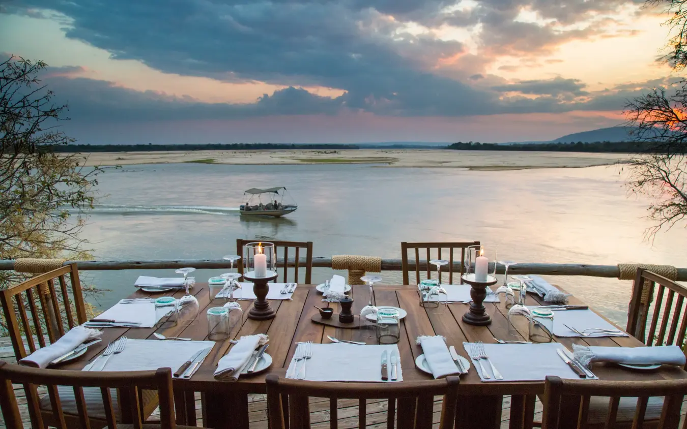 Waterfront dining table set for dinner at sunset overlooking river, Sand Rivers, Nyerere National Park, Tanzania