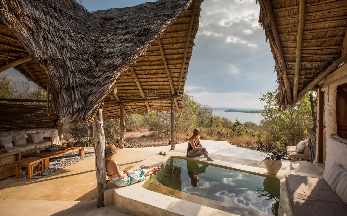 Guests relaxing by infinity pool with lake view from thatched safari lodge, Sand Rivers, Nyerere National Park, Tanzania
