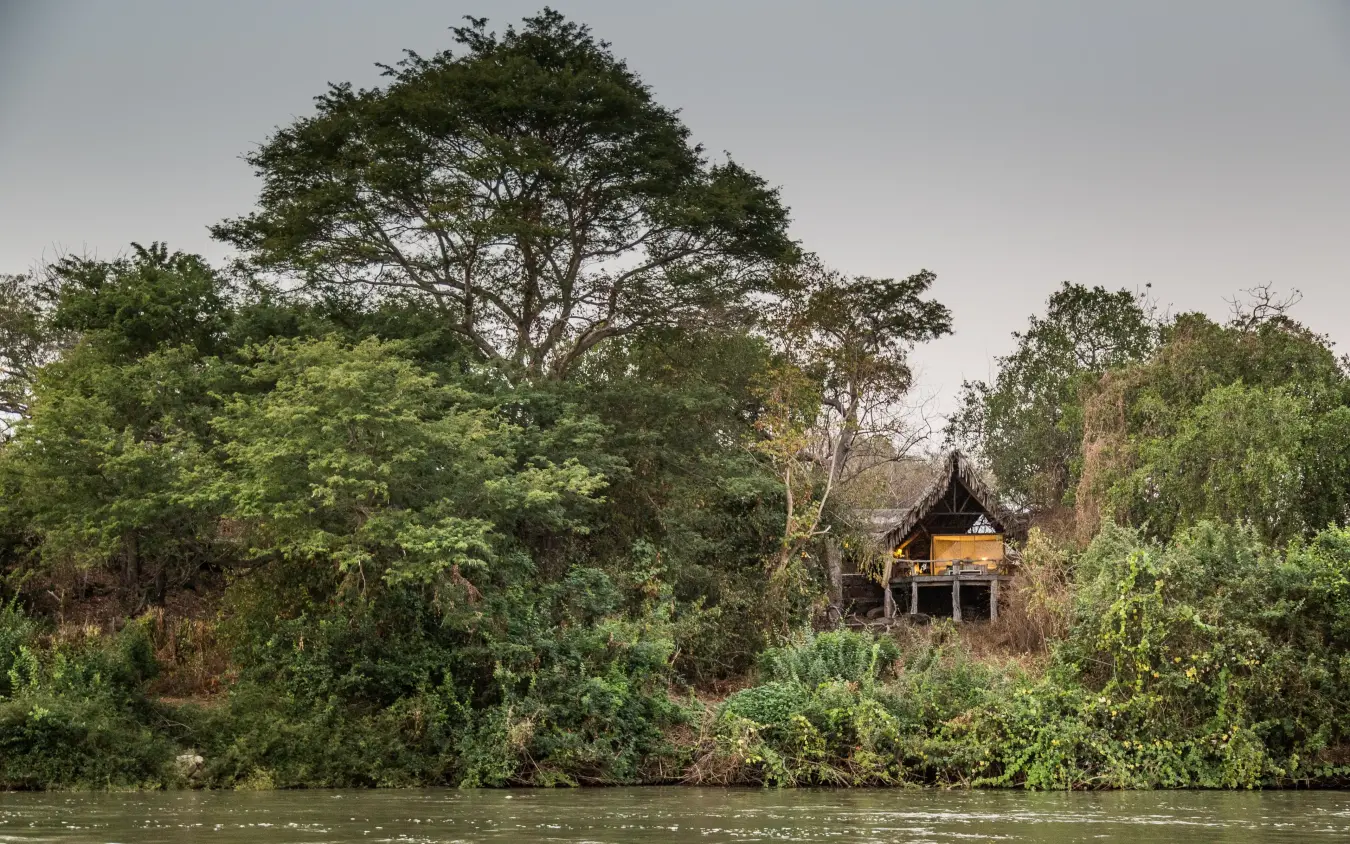 Traditional wooden lodge nestled among riverside trees and vegetation, Sand Rivers, Nyerere National Park, Tanzania