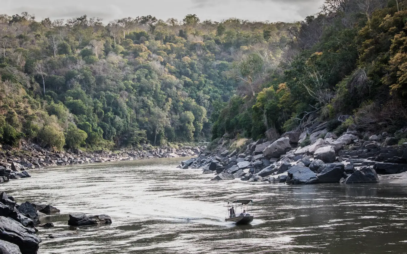 Small boat on river with forested gorge and rocky banks, Sand Rivers, Nyerere National Park, Tanzania