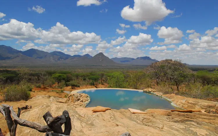 Natural water pool surrounded by savanna and distant mountains, Sarara Camp, Northern Kenya, Kenya
