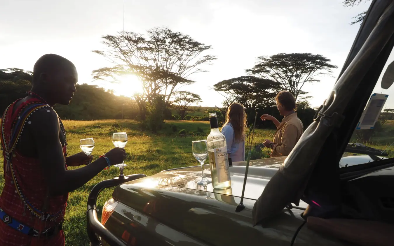 Guests enjoy sunset drinks served from vehicle in savanna, Eagle View Camp, Maasai Mara, Kenya