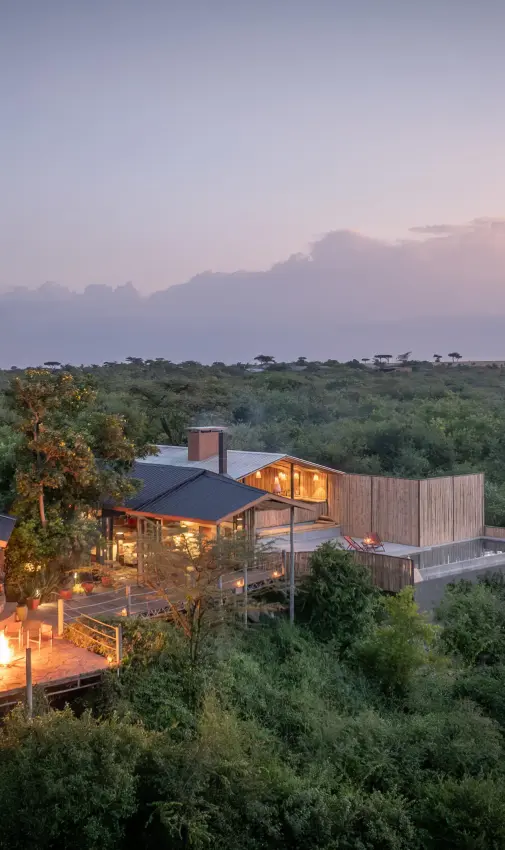 Illuminated lodge structures nestled in savanna landscape at dusk, Eagle View Camp, Maasai Mara, Kenya