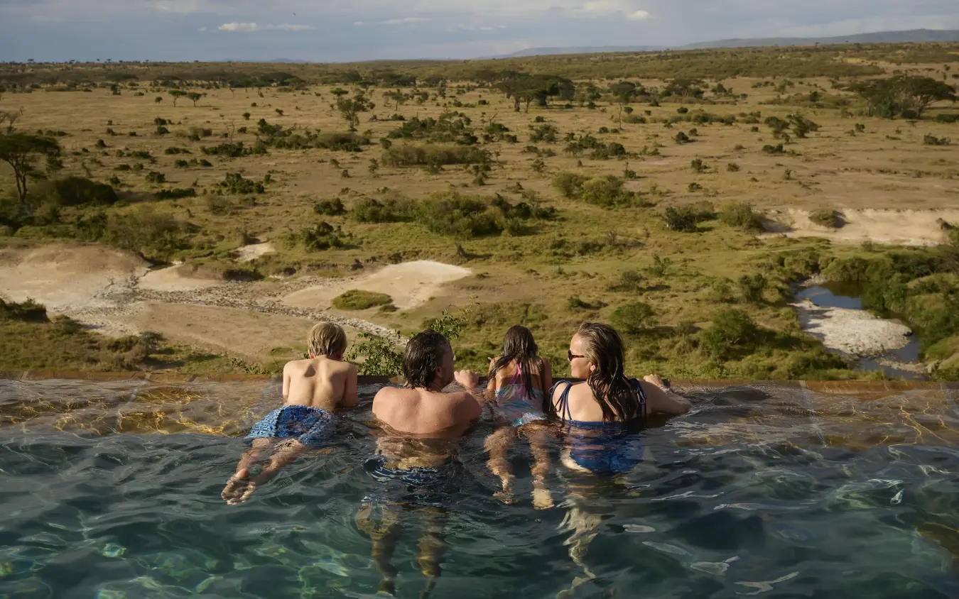 Guests swimming in infinity pool overlooking savanna landscape, Eagle View Camp, Maasai Mara, Kenya