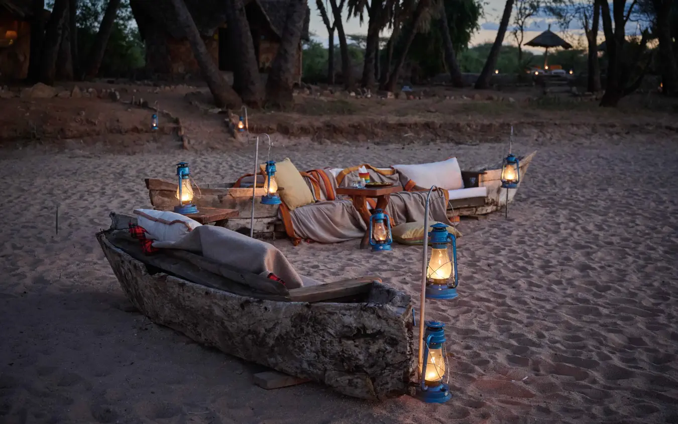 Beachside dining setup with canoes and lanterns on sand at dusk, Saruni Rhino, Northern Kenya, Kenya
