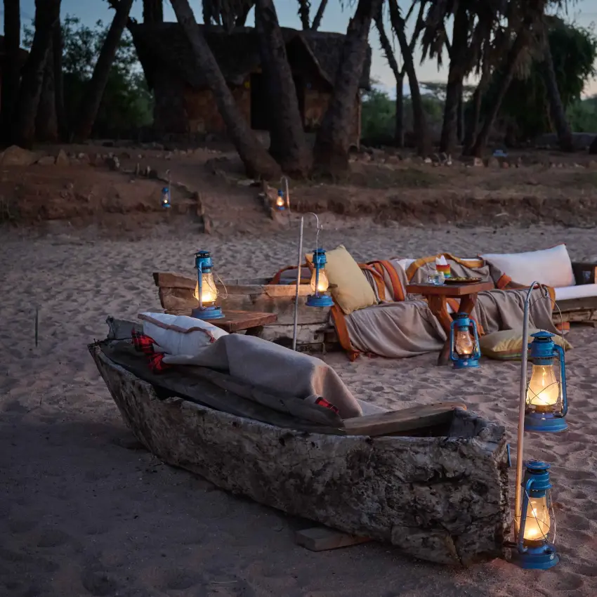 Beachside dining setup with canoes and lanterns on sand at dusk, Saruni Rhino, Northern Kenya, Kenya
