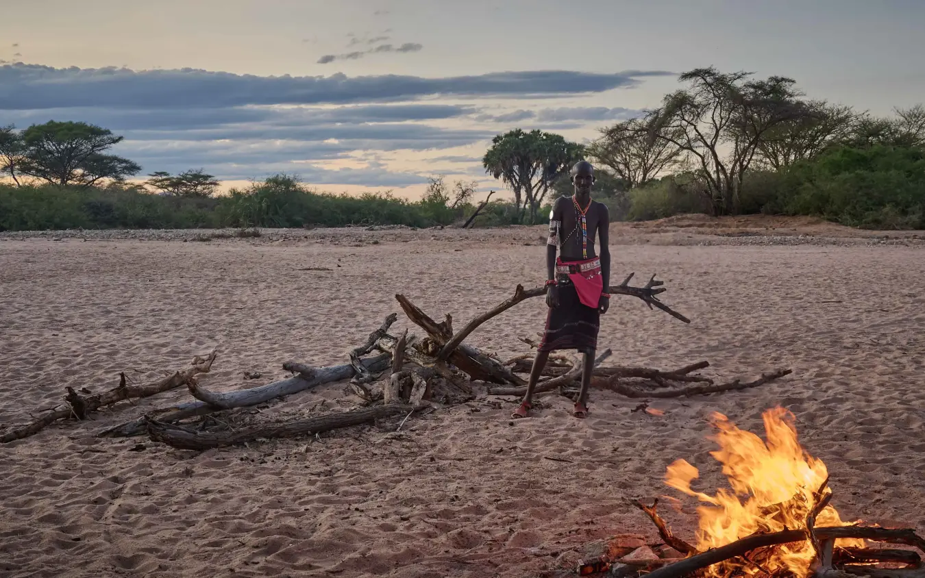 Person standing by campfire on sandy riverbed at dusk, Saruni Rhino, Northern Kenya, Kenya