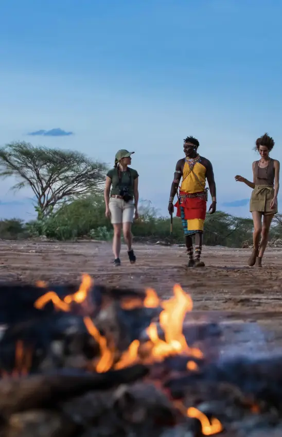 Three hikers walking near campfire on savanna at dusk, Saruni Rhino, Northern Kenya, Kenya