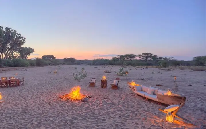 Campfire with torch-lit seating on sandy ground at dusk, Saruni Rhino, Northern Kenya, Kenya
