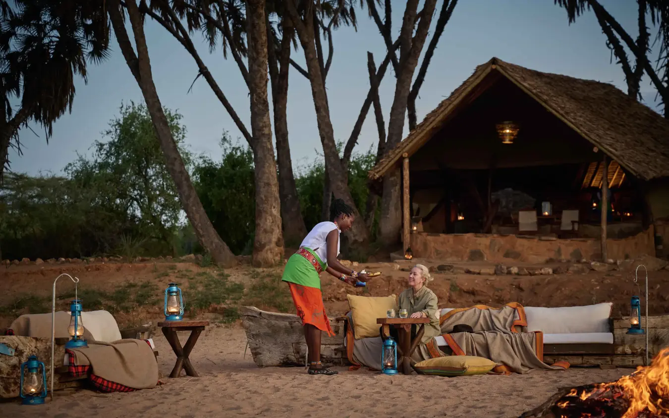 Staff serving drinks to guest at safari camp firesite at dusk, Saruni Rhino, Northern Kenya, Kenya