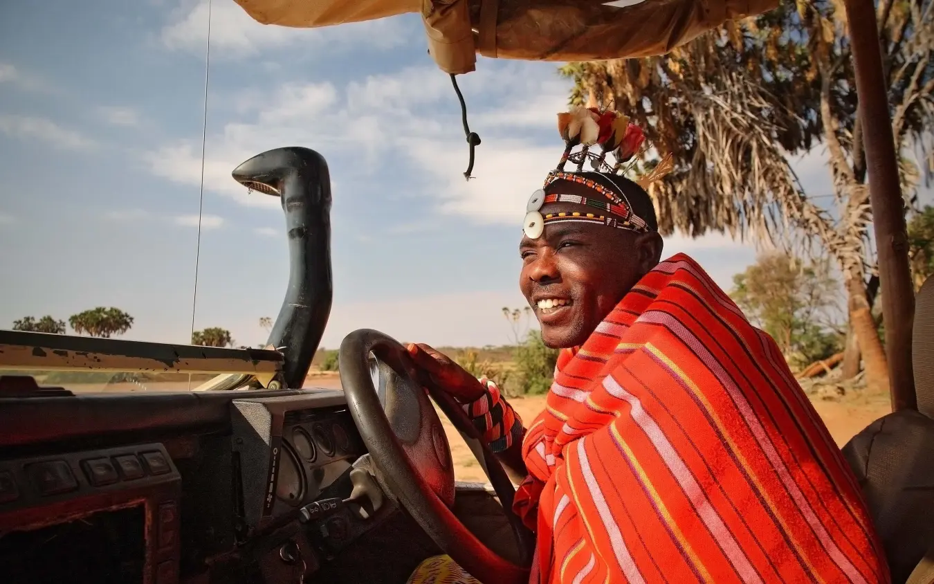 Maasai warrior at vehicle steering wheel wearing traditional red shawl and beaded headdress, Saruni Rhino, Northern Kenya, Kenya