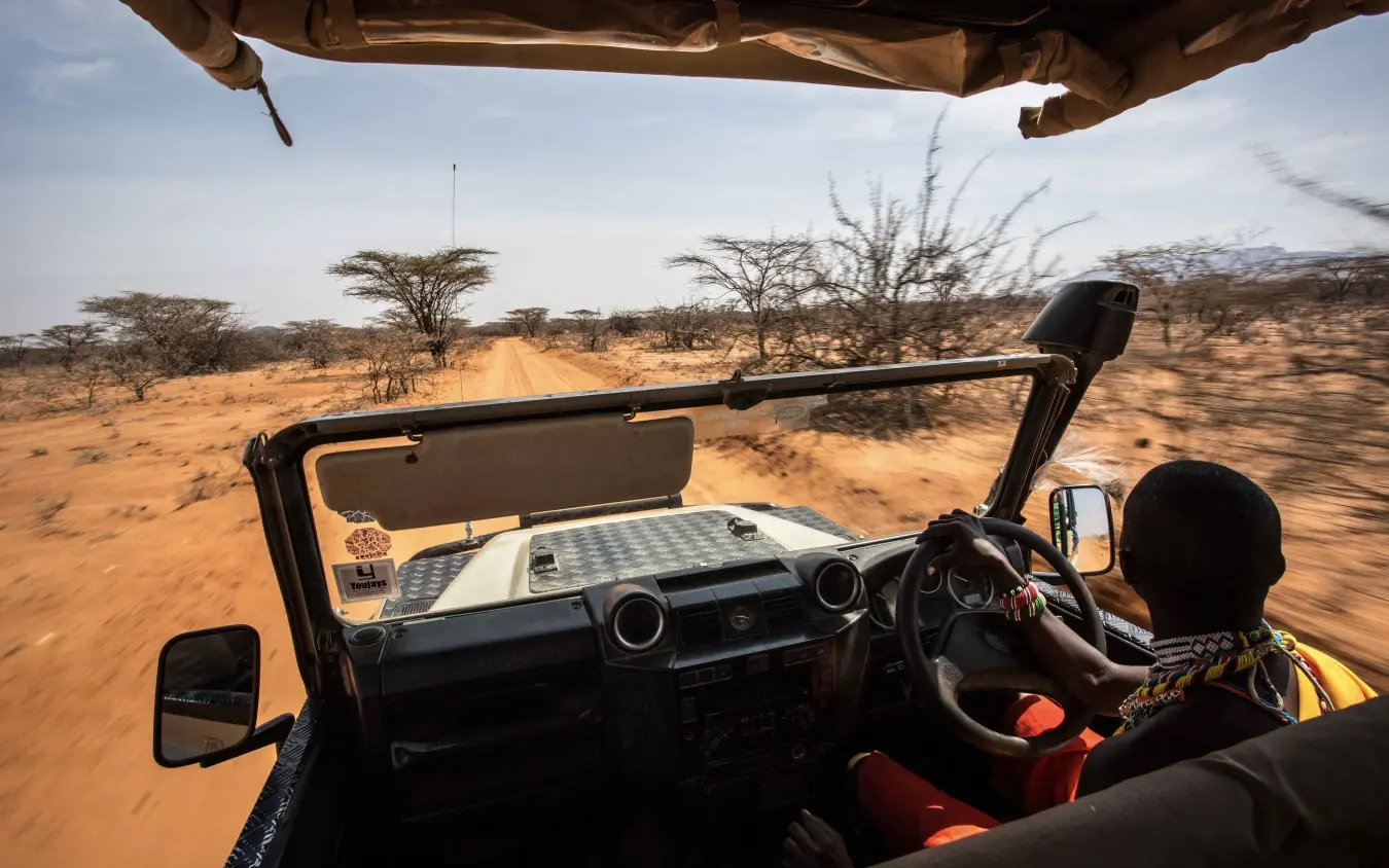 Open-top safari vehicle driving on dusty track through arid bushland, Saruni Rhino, Northern Kenya, Kenya