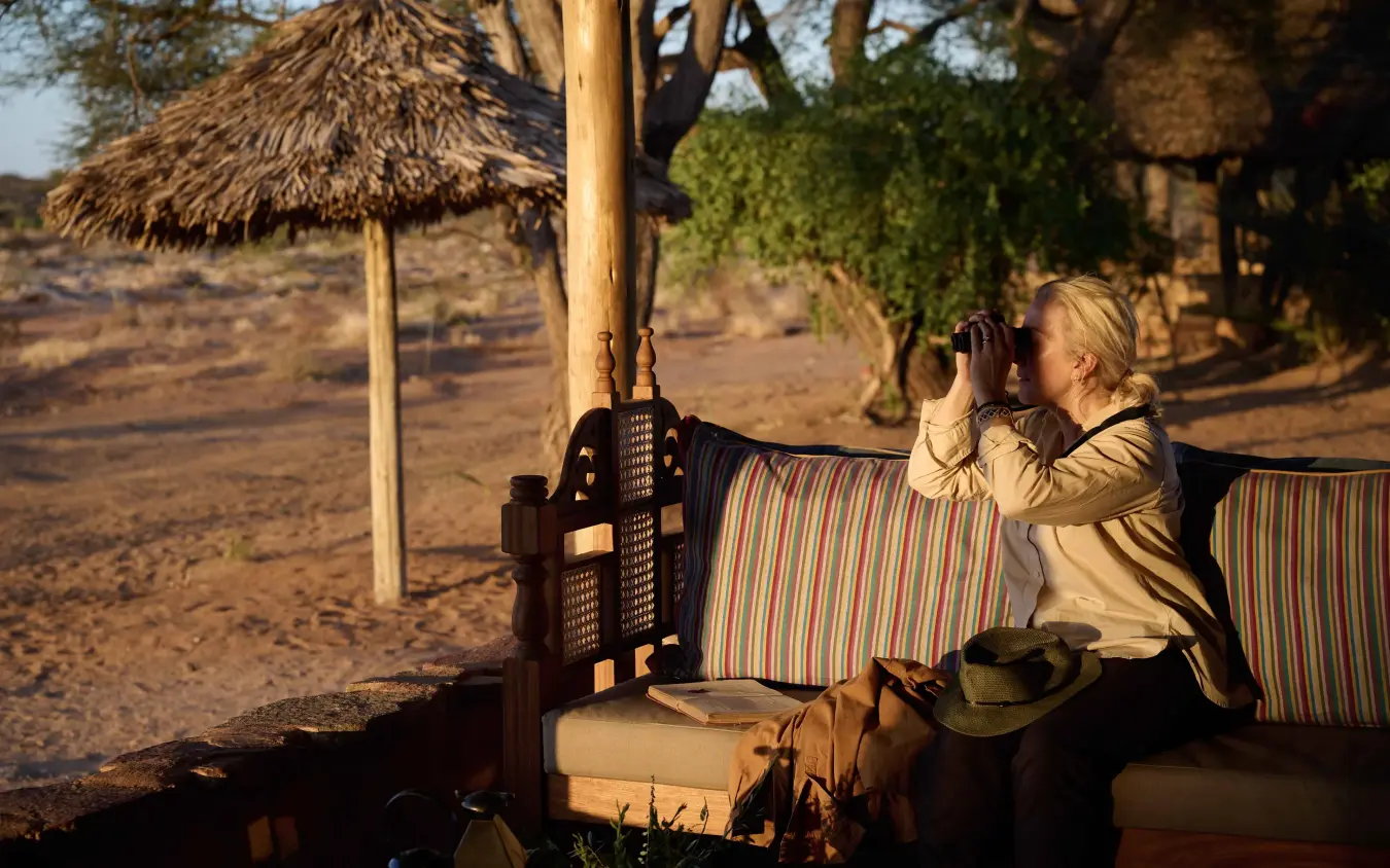 Guest with binoculars viewing wildlife from shaded lounge area at safari camp, Saruni Rhino, Northern Kenya, Kenya