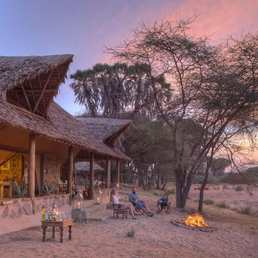 Thatched lodge with firepit and guests at sunset in arid savanna landscape, Saruni Rhino, Northern Kenya, Kenya