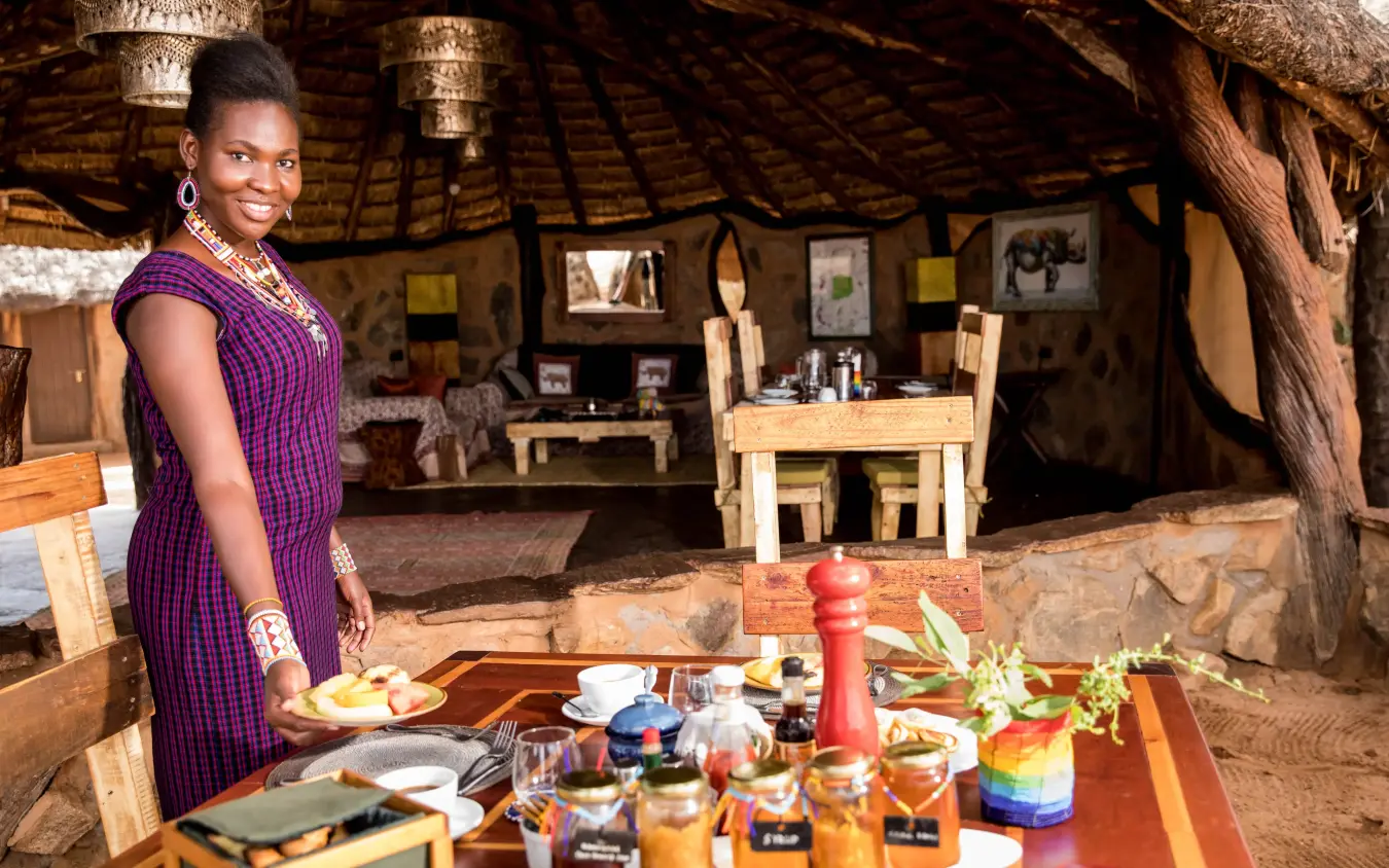 Woman serving meal at traditional thatched-roof lodge dining area, Saruni Rhino, Northern Kenya, Kenya