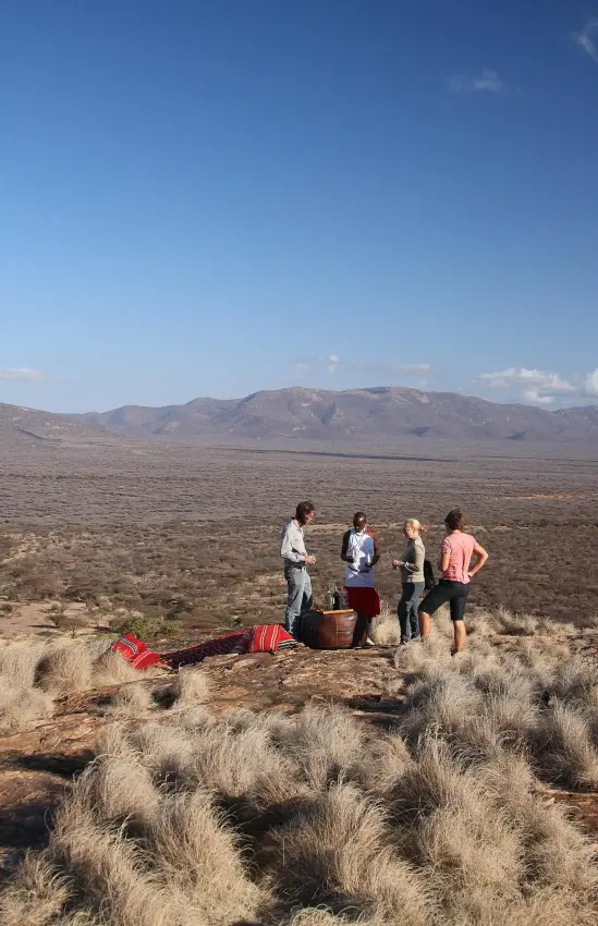 Guests gathered on rocky outcrop overlooking vast savanna landscape, Samburu Reserve, Kenya