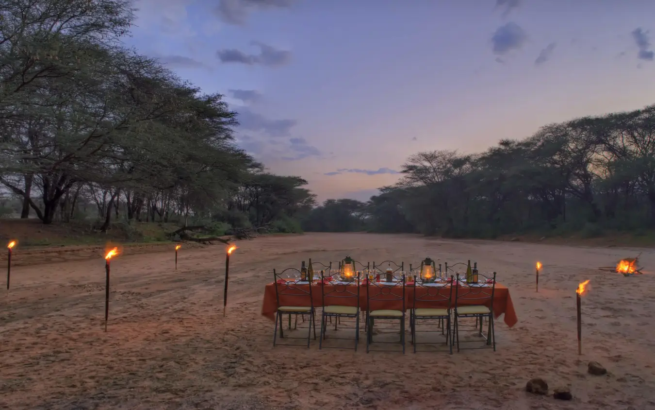 Desert dining setup with torches at dusk under acacia trees, Saruni Samburu, Samburu Reserve, Kenya