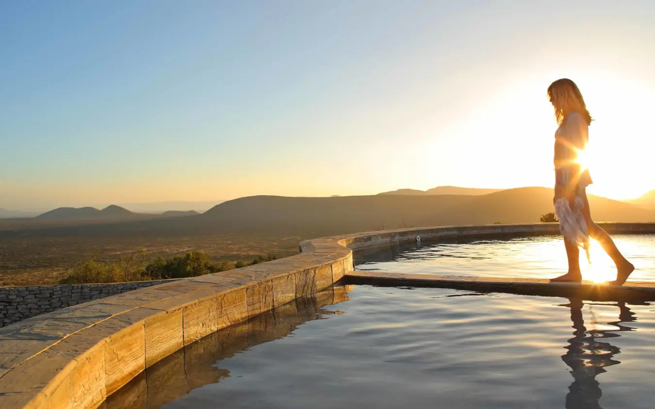 Woman at infinity pool overlooking African savanna at sunset, Saruni Samburu, Samburu Reserve, Kenya