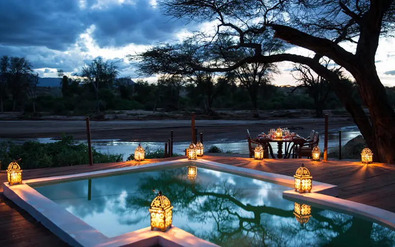 Illuminated pool overlooking river at twilight with lanterns, Sasaab, Samburu Reserve, Kenya