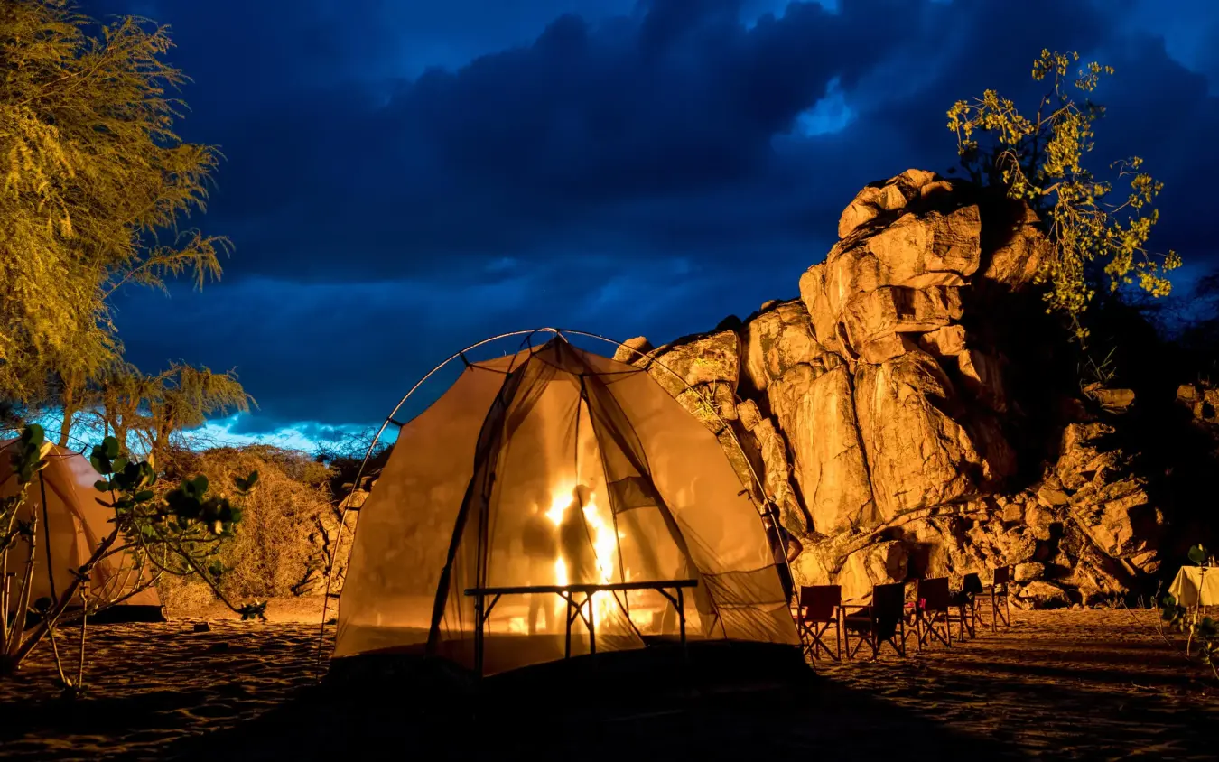 Illuminated tent camp beside rocky outcrop at dusk, Sasaab, Samburu Reserve, Kenya