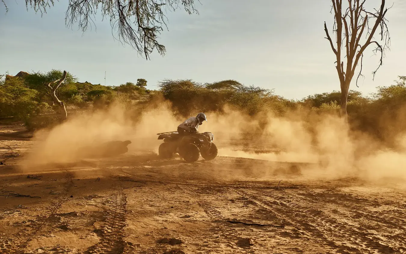Person riding all-terrain vehicle through dusty desert landscape, Sasaab, Samburu Reserve, Kenya