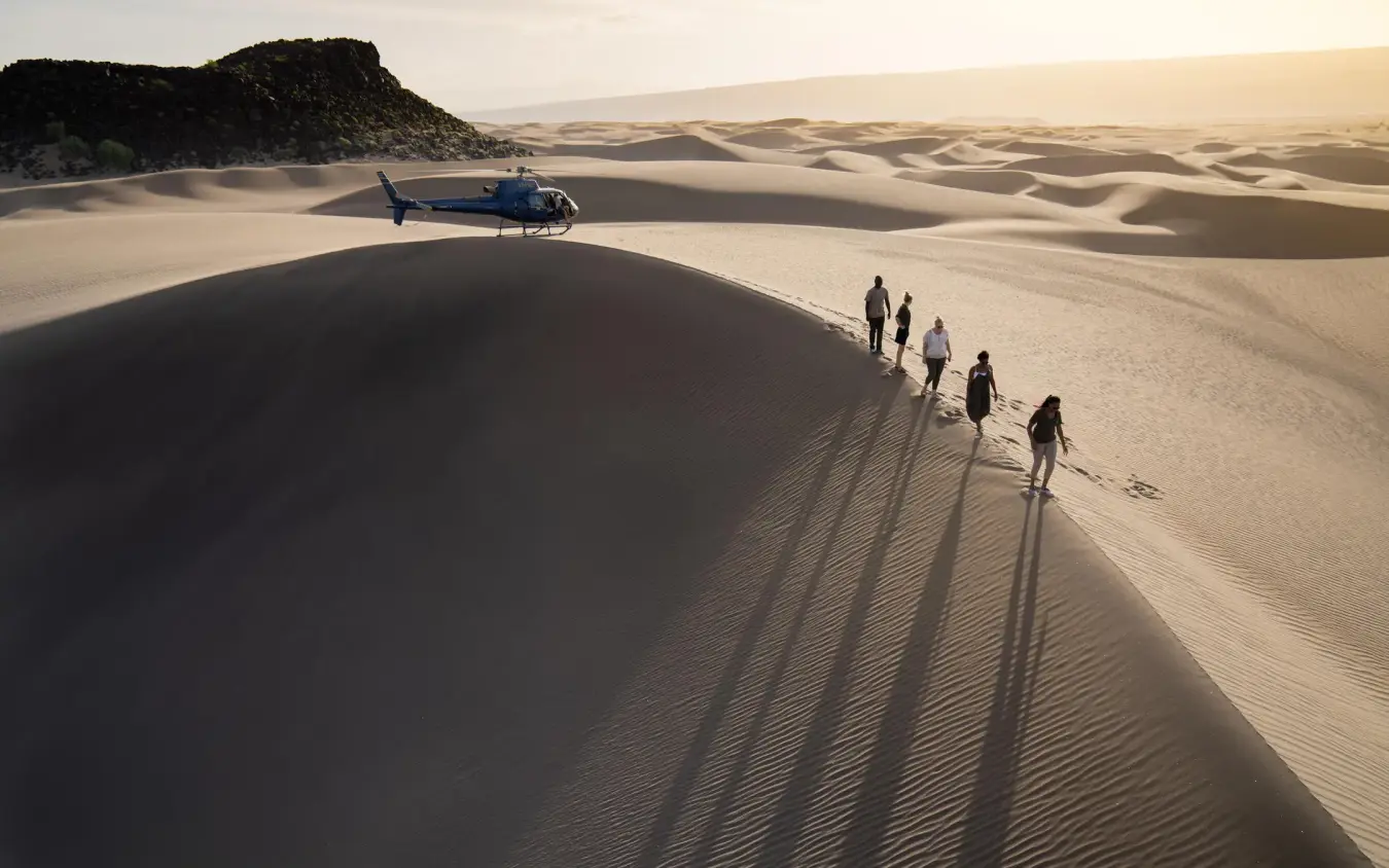 Group of guests walking toward helicopter in desert dunes, Sasaab, Samburu Reserve, Kenya