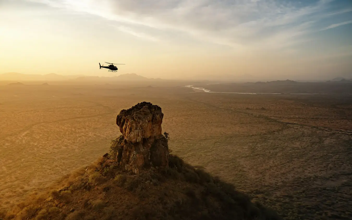 Helicopter flying over rocky outcrop in arid landscape, Sasaab, Samburu Reserve, Kenya