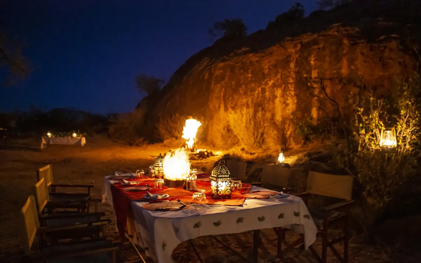 Outdoor dining setup under rock formation at dusk, Sasaab, Samburu Reserve, Kenya
