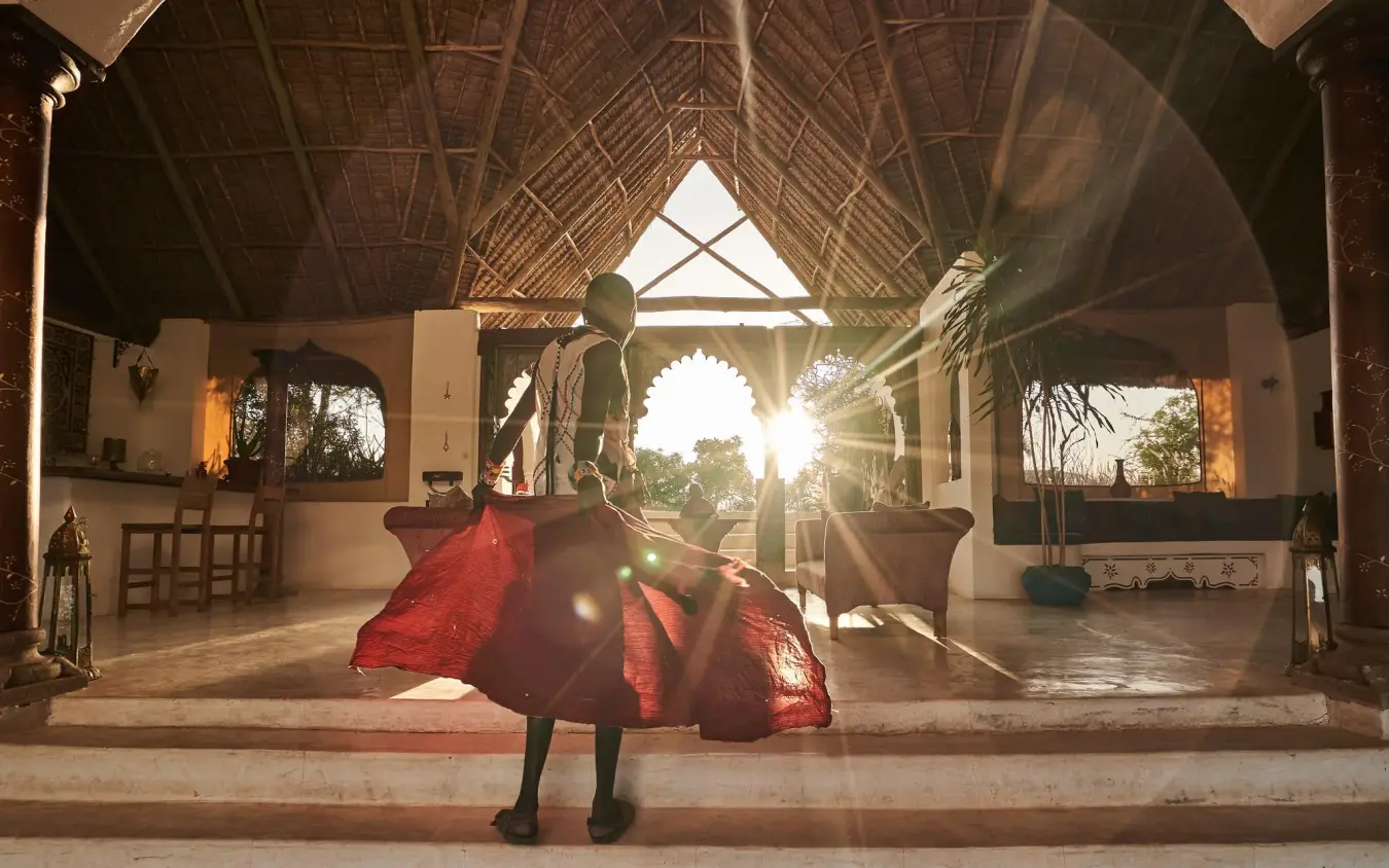 Person in red fabric standing in open-sided lodge at sunset, Sasaab, Samburu Reserve, Kenya