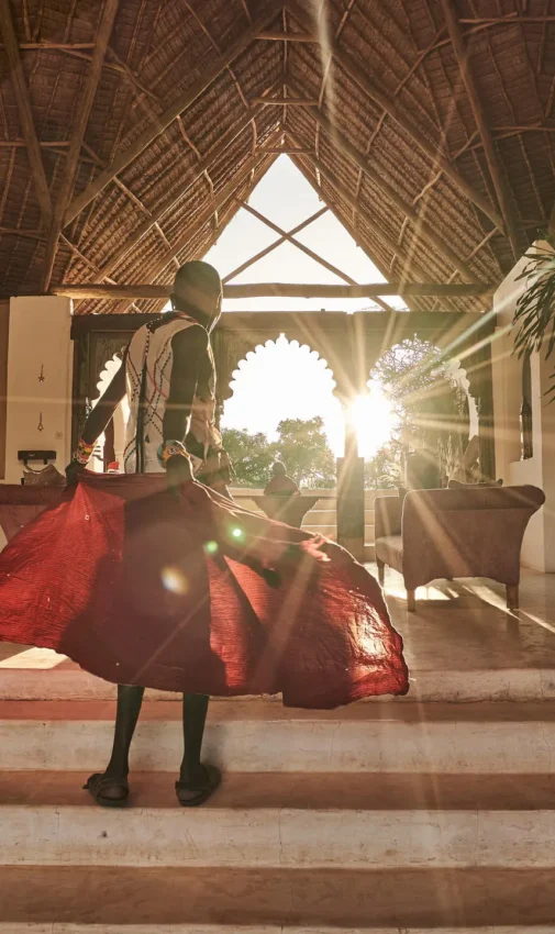 Person in red fabric standing in open-sided lodge at sunset, Sasaab, Samburu Reserve, Kenya