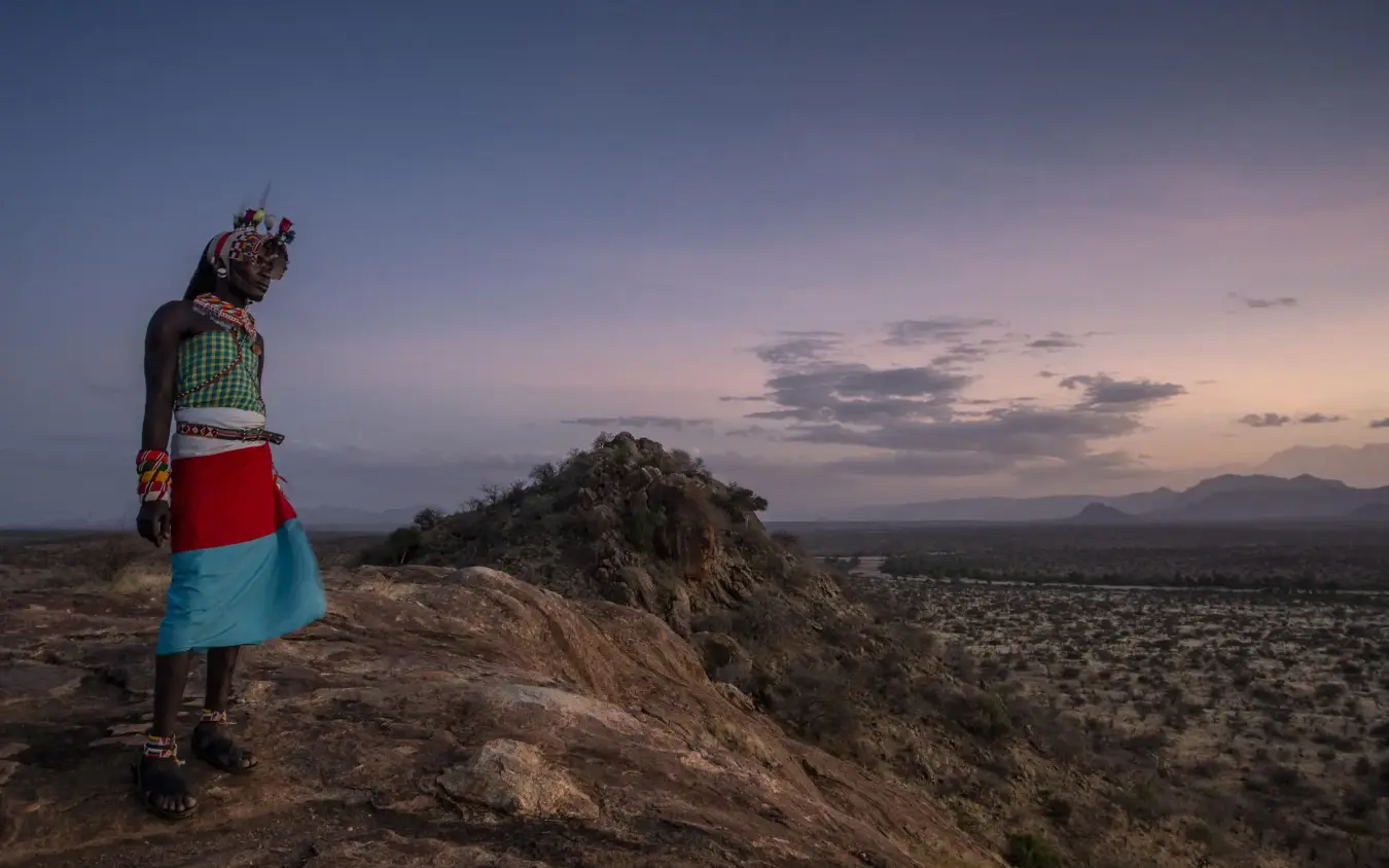 Maasai warrior standing on rocky outcrop at sunset, Kenya