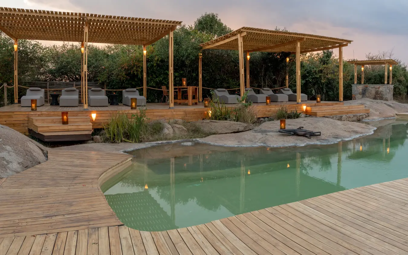 Wooden deck surrounding natural pool with pergolas and lounging areas, Sayari Camp, Serengeti National Park, Tanzania