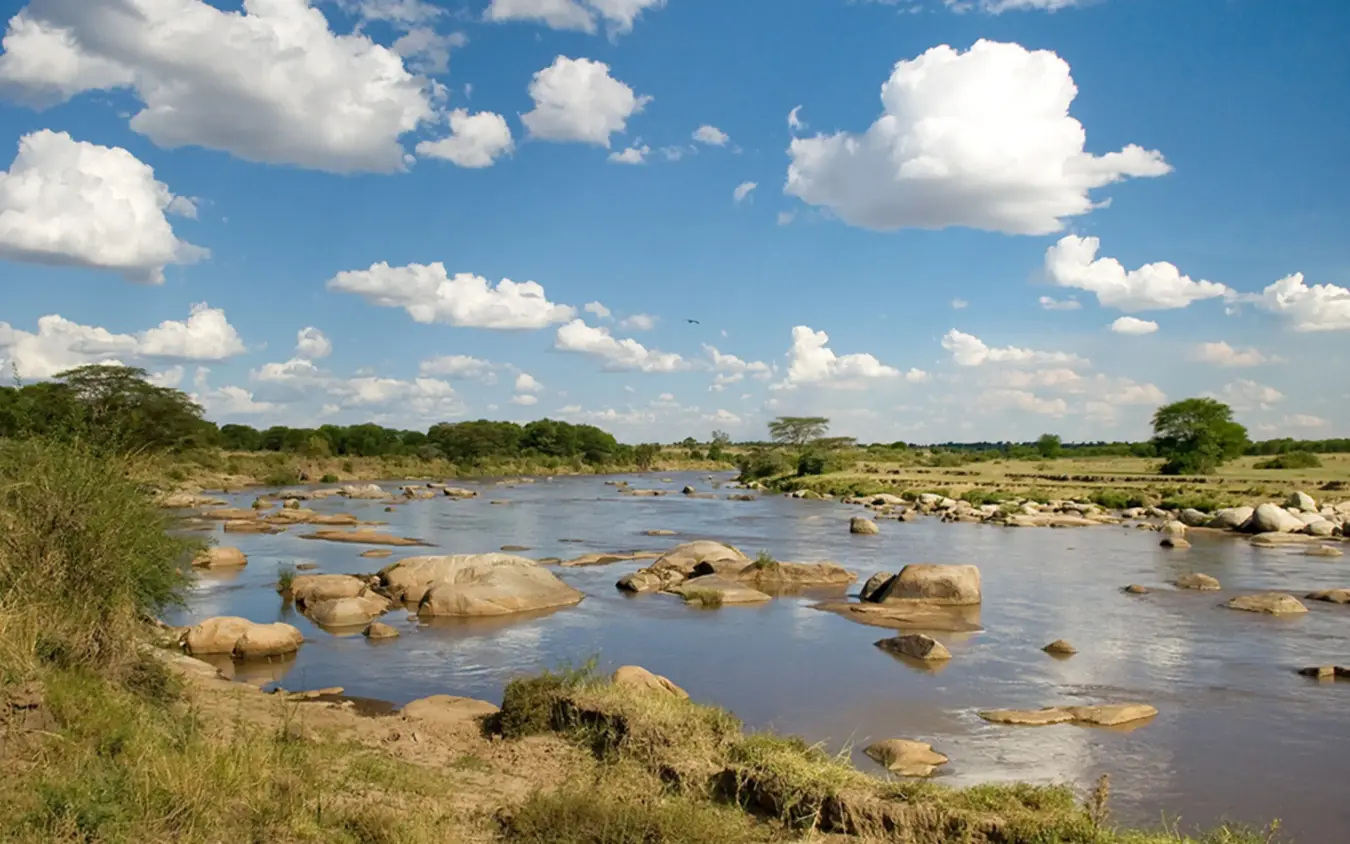 River landscape with boulders under blue sky and clouds, Sayari Camp, Serengeti National Park, Tanzania