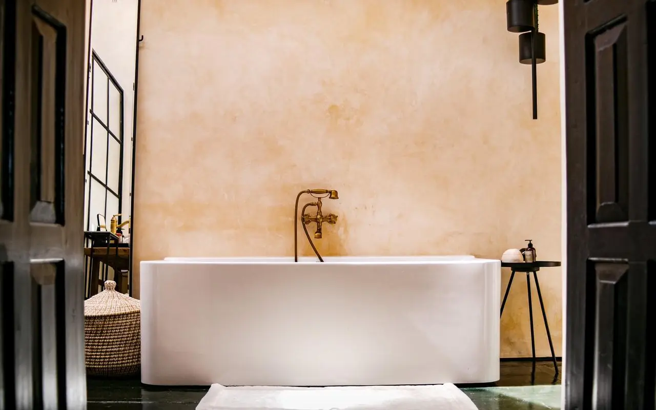 Modern white bathtub with brass fixtures against textured wall, Segera, Laikipia Highlands, Kenya