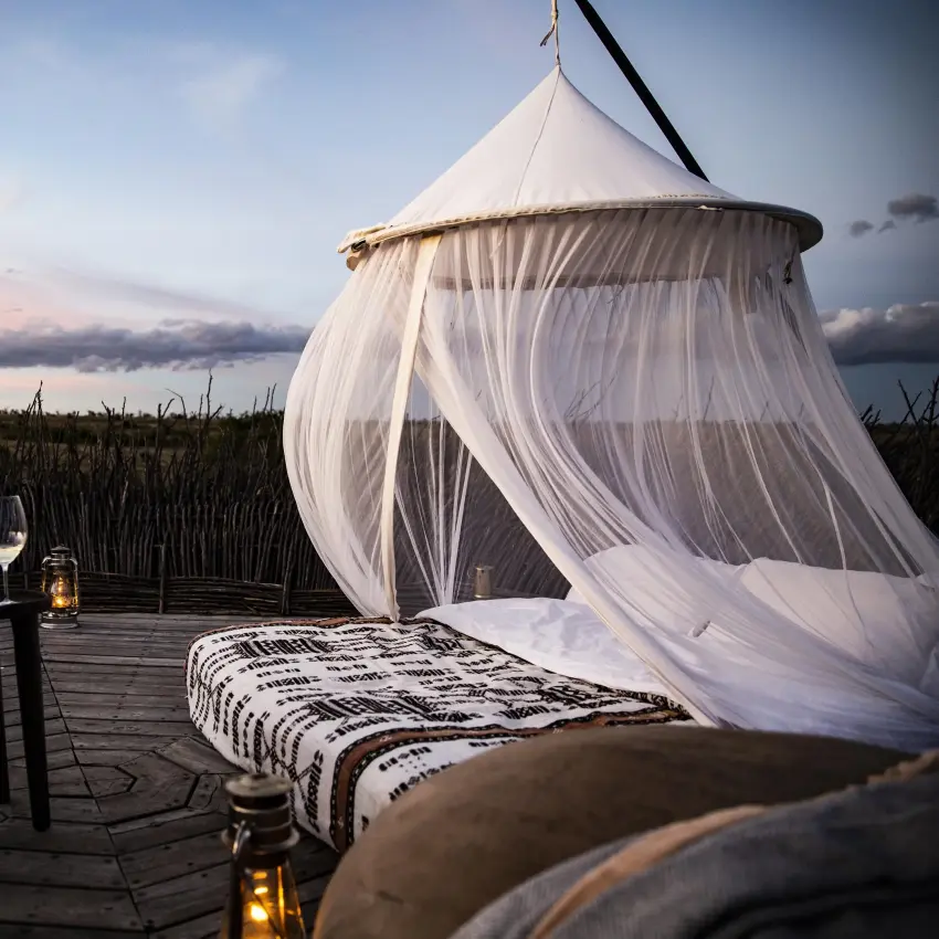 Canopied bed on wooden deck at sunset overlooking wetland, Segera, Laikipia Highlands, Kenya