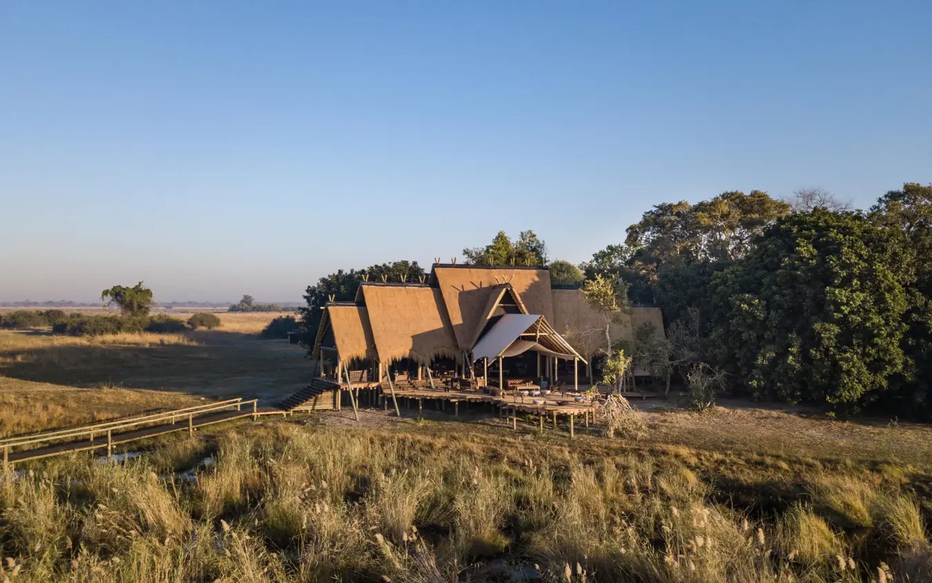 Thatched-roof lodge buildings in savanna landscape at sunset, Selinda Camp, Selinda Reserve, Botswana