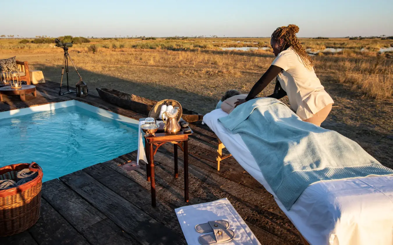 Guest relaxing by pool overlooking savanna landscape, Selinda Camp, Selinda Reserve, Botswana