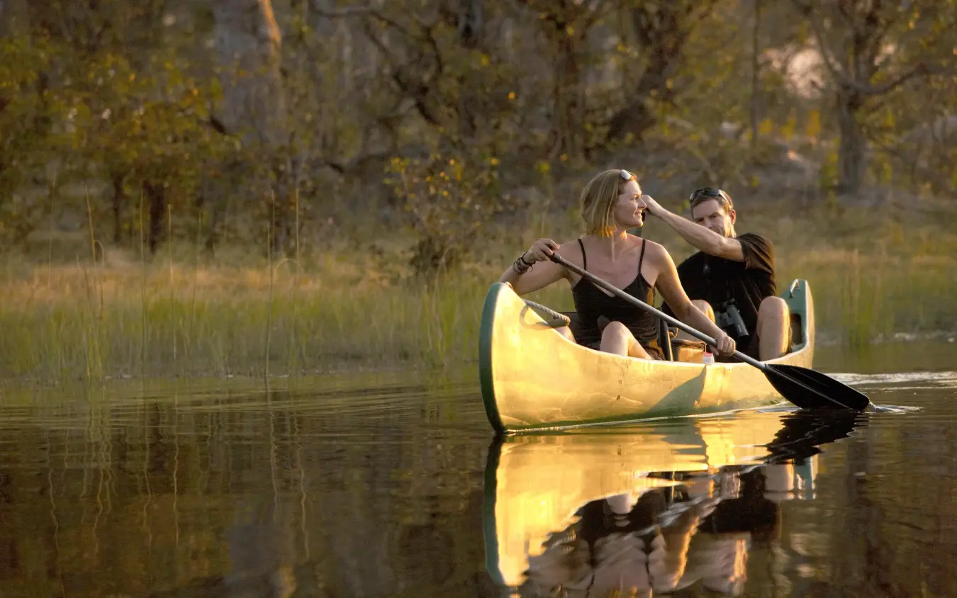 Two guests paddling yellow canoe on calm river at sunset, Selinda Explorers Camp, Selinda Reserve, Botswana