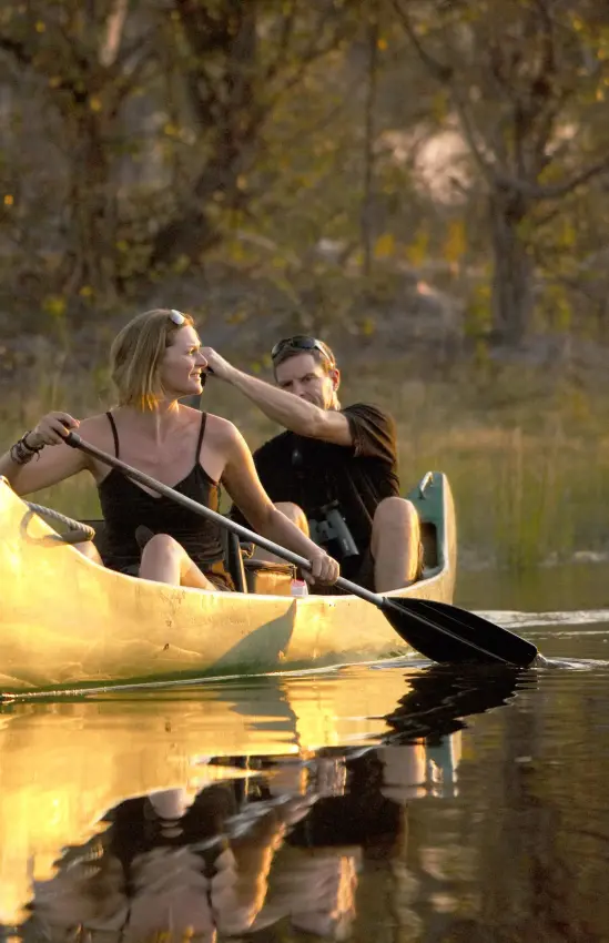 Two guests paddling yellow canoe on calm river at sunset, Selinda Explorers Camp, Selinda Reserve, Botswana
