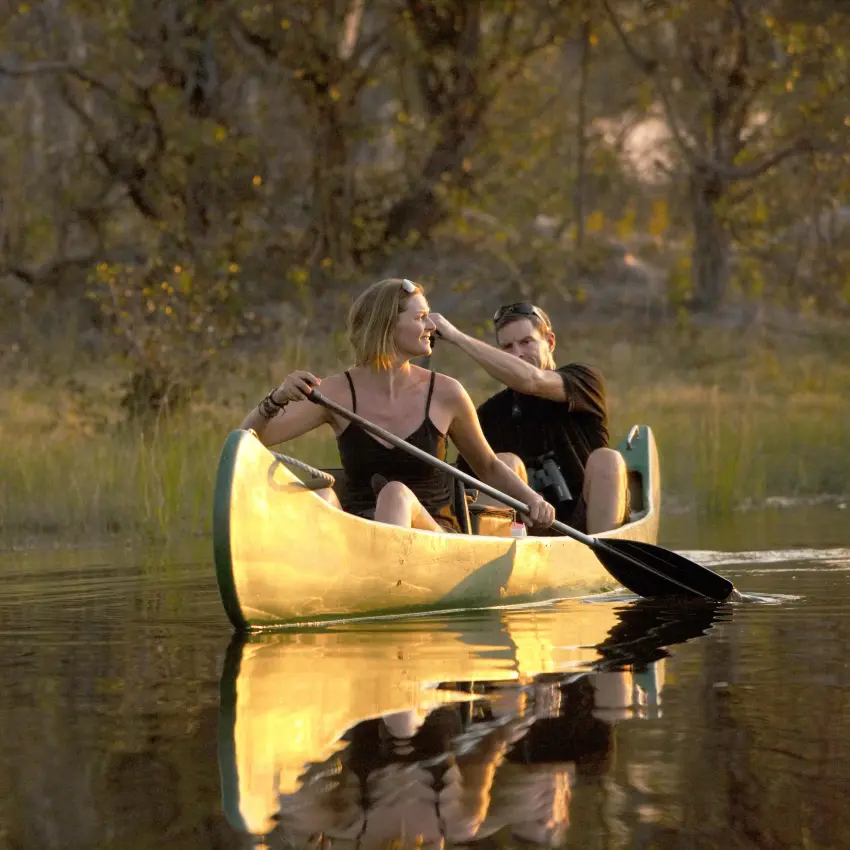 Two guests paddling yellow canoe on calm river at sunset, Selinda Reserve, Botswana